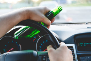 image of a person with an open beer bottle, driving while drinking